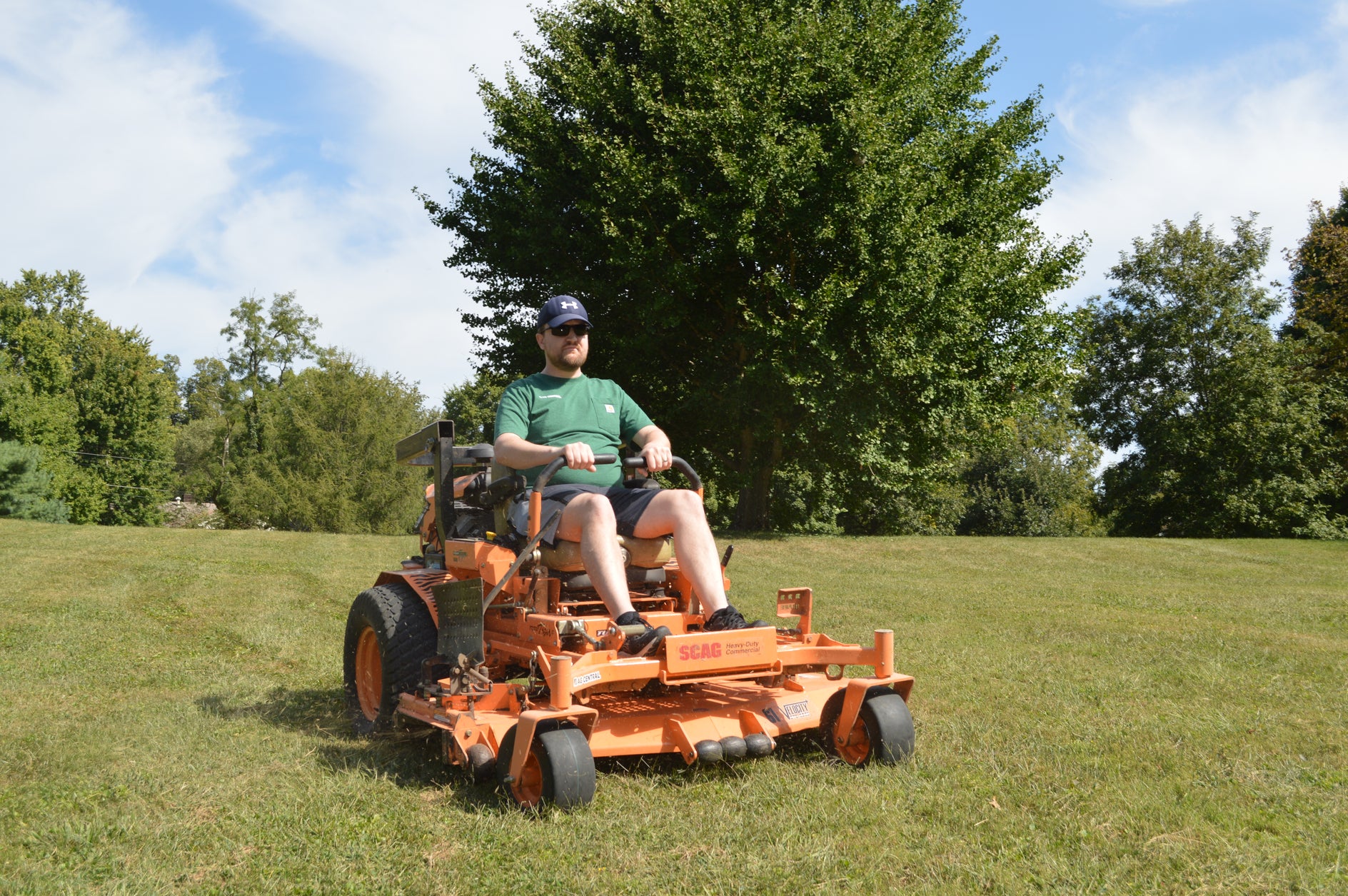 Man operating a riding lawn mower in a grassy area with trees in the background